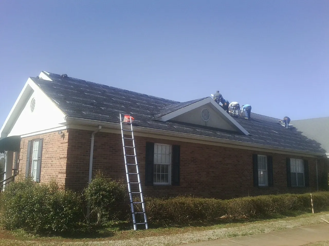 Crew tearing shingles off a brick ranch roof with a ladder set — Metal Roof Repair work by our crew in Claysburg