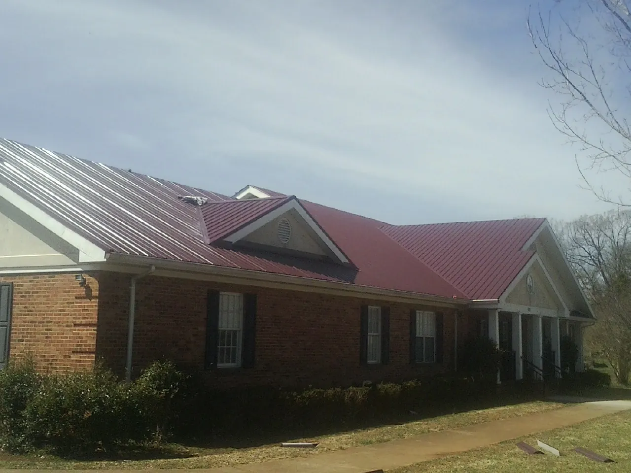 Red metal roof with gabled entries on a long brick building, from a Hail Damage Roof Repair job in Claysburg