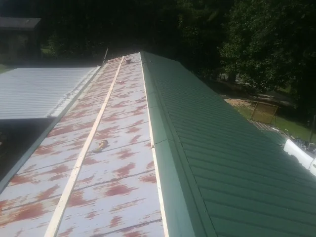 Old rusted panels beside newly installed green metal roofing — Wind Damage Roof Repair by Roofing Brothers in Claysburg