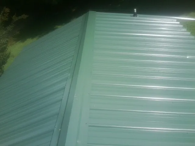 New green metal panels meeting at the ridge of a roof — Flat Roof Repair work by our crew in Claysburg