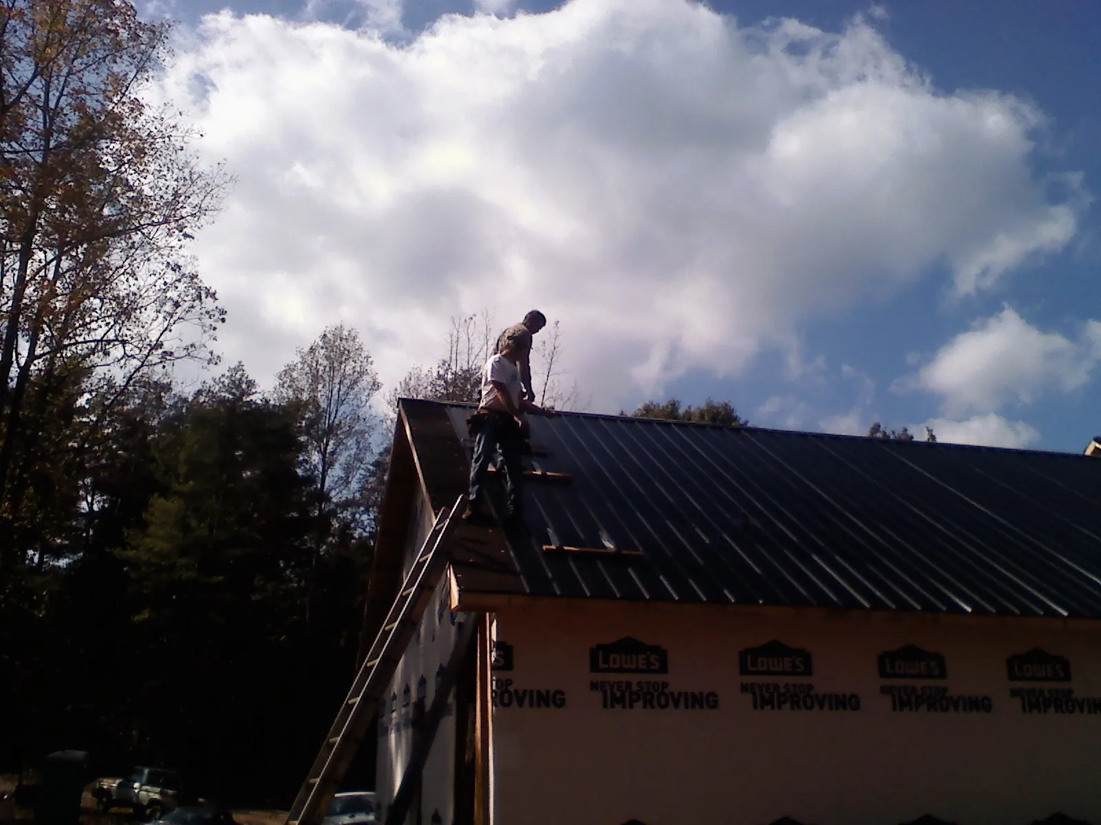 Roofer fastening dark metal panels high against a cloudy sky, from a Roof Inspection job in Claysburg