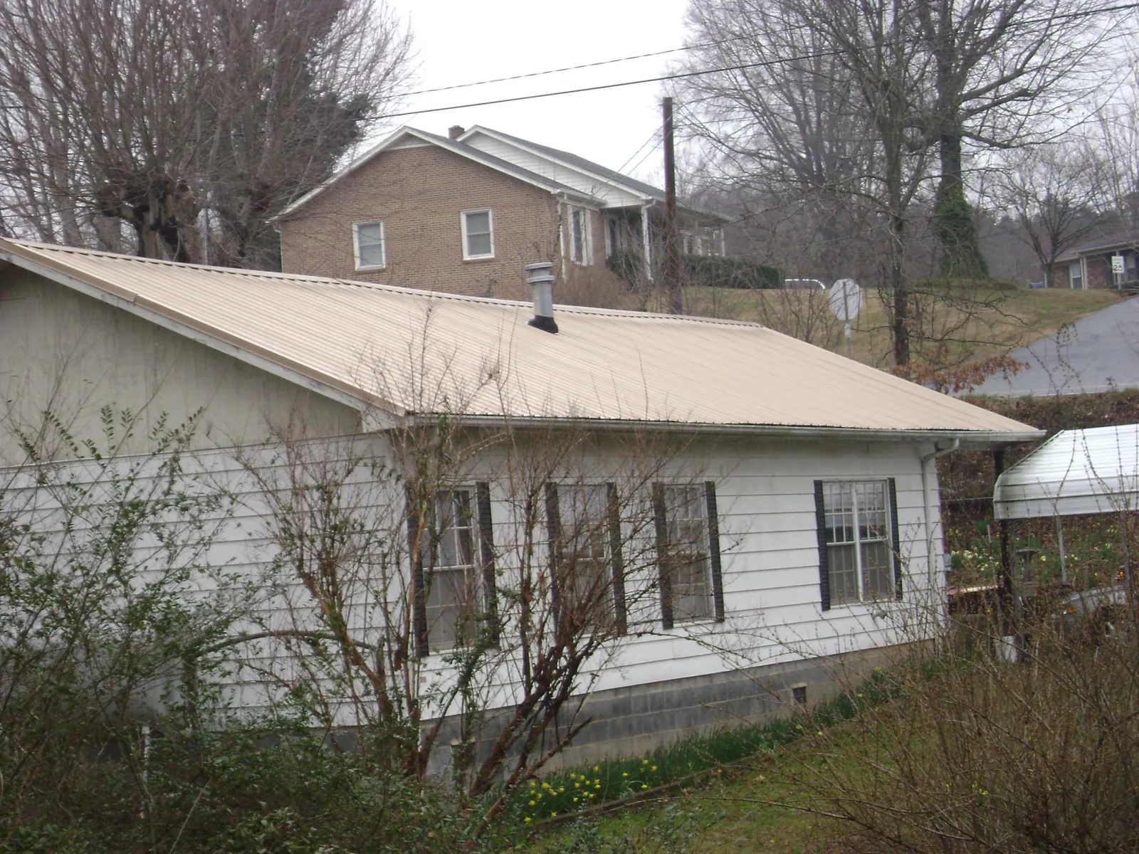 Tan metal roof on a white sided house set into a hillside — Commercial Roofing by Roofing Brothers in Claysburg