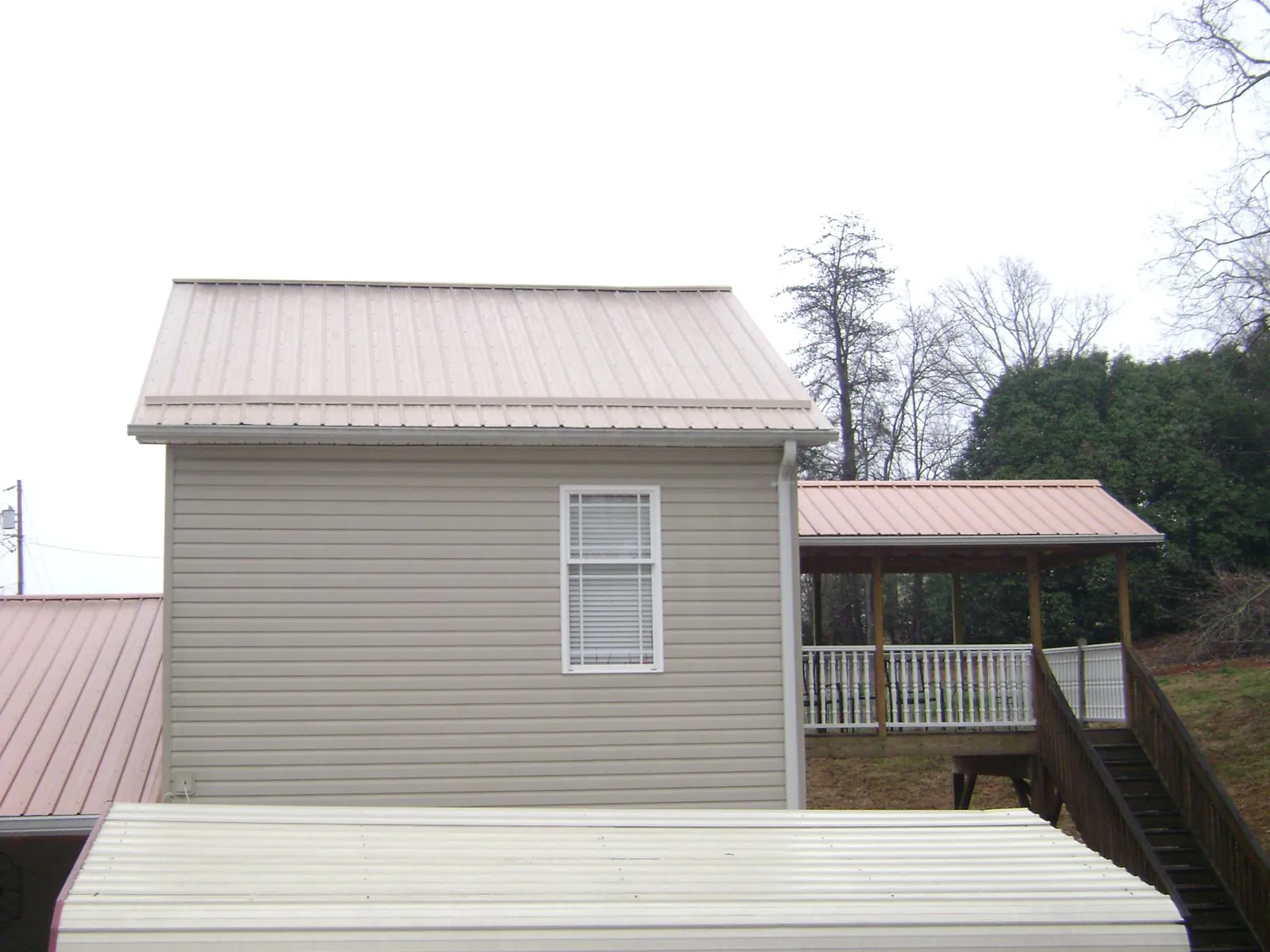 Tan metal roofs on a two story addition and attached porch, from a Roof Replacement job in Claysburg